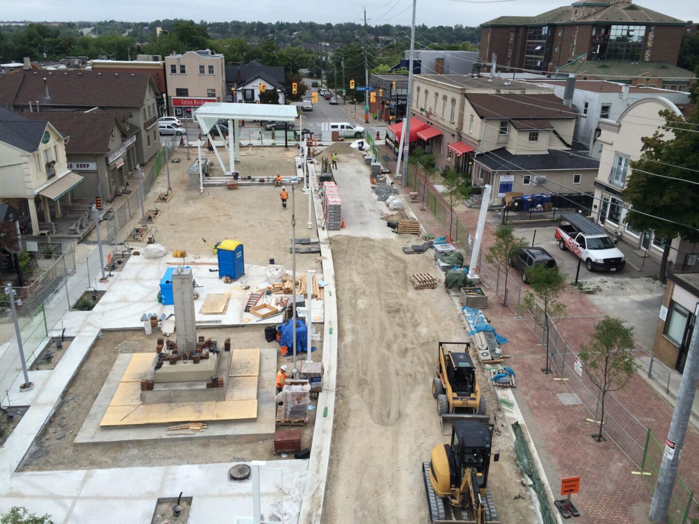 Aerial view of an urban construction site with heavy machinery, materials scattered around, and buildings in the surrounding area.