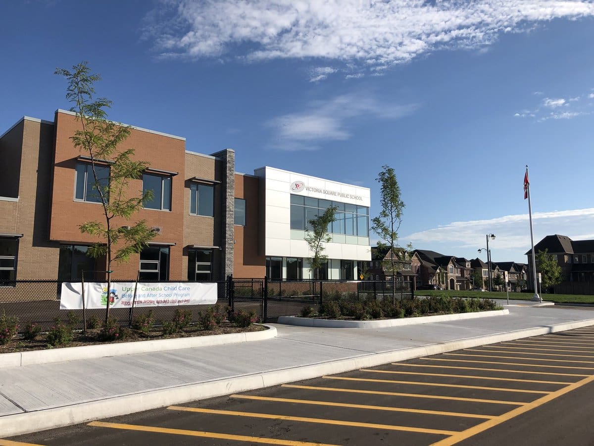 A modern elementary school building with a parking lot in the foreground under a clear blue sky.