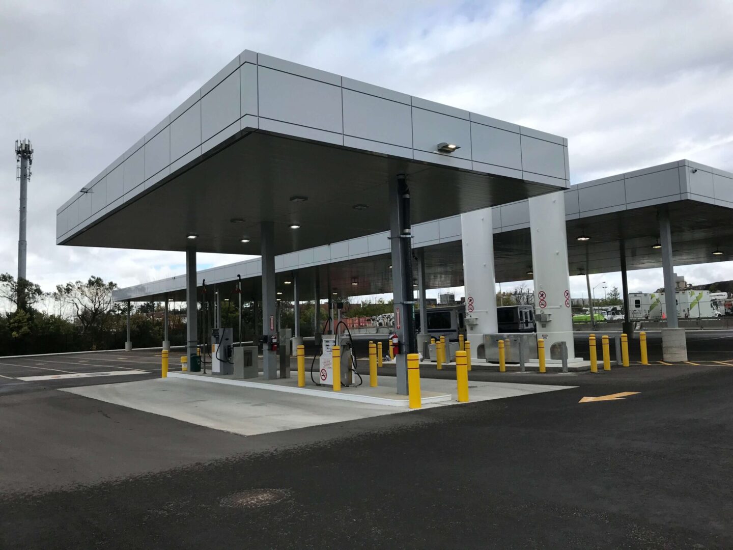 A modern toll booth plaza with multiple lanes, canopy overhead, and yellow safety bollards, under an overcast sky.