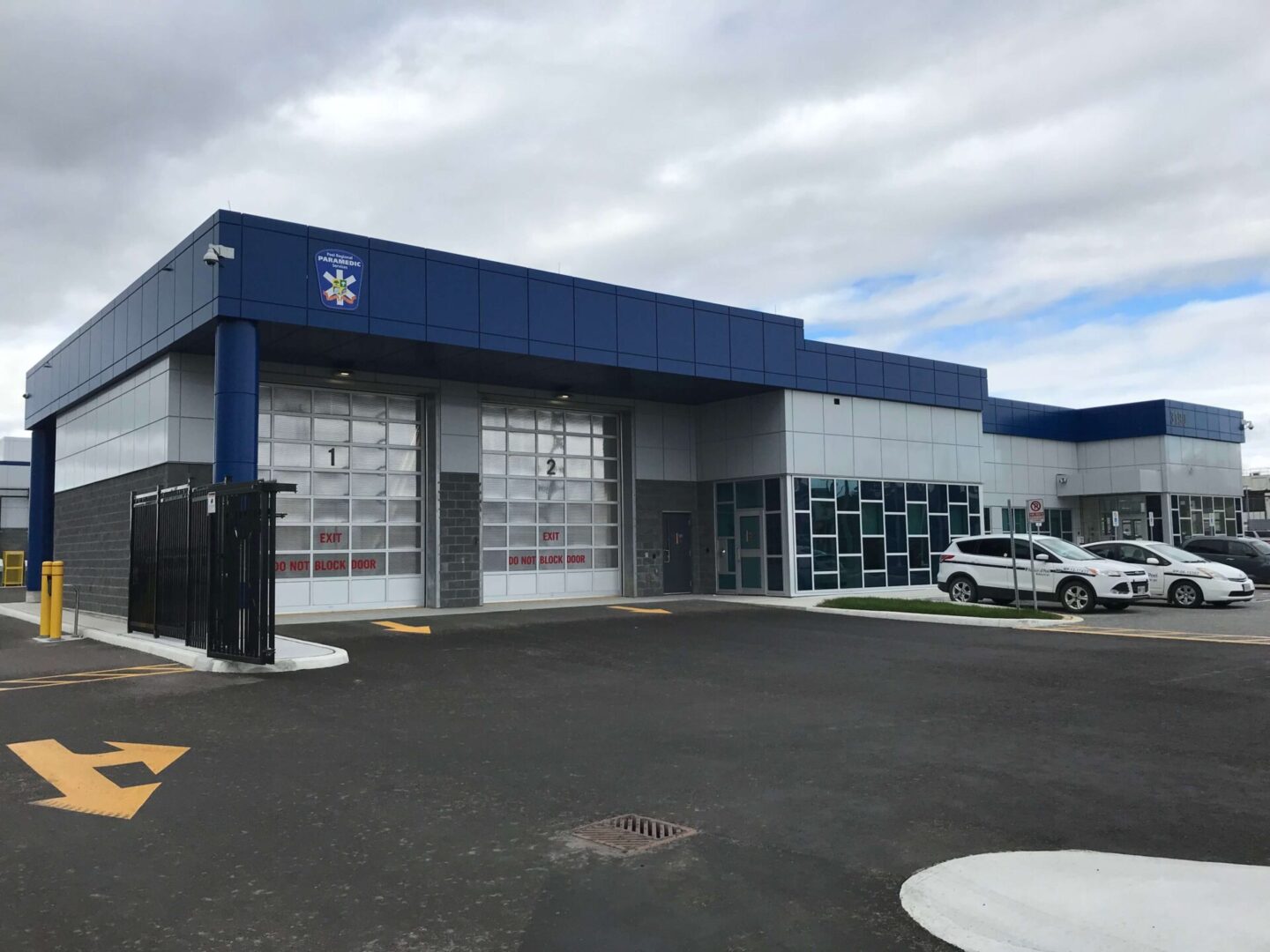 Exterior view of a modern fire station with blue and gray facade, featuring large garage doors and a parking lot with vehicles.