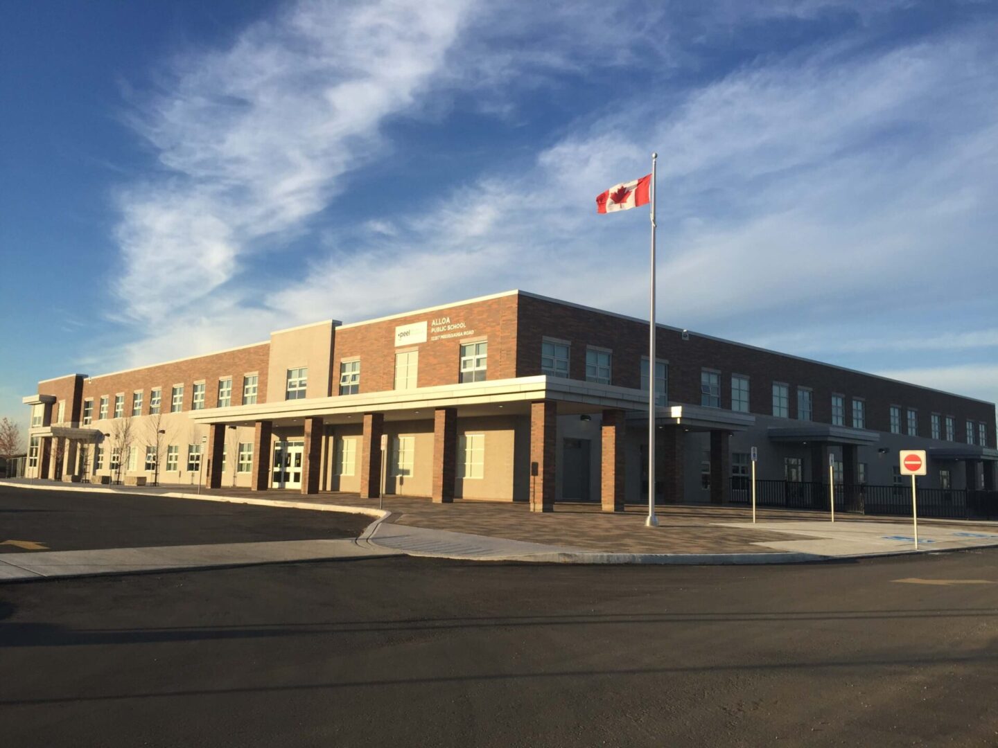 A modern school building with a Canadian flag waving on a flagpole, set against a clear blue sky.