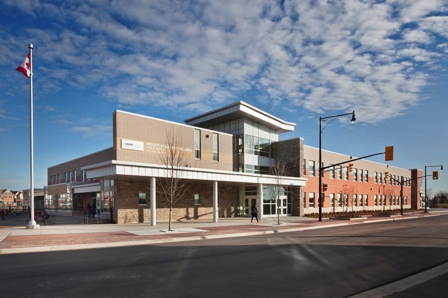 Modern community center with brick facade, large windows, Canadian flag, and clear blue sky, located at an intersection on a sunny day.