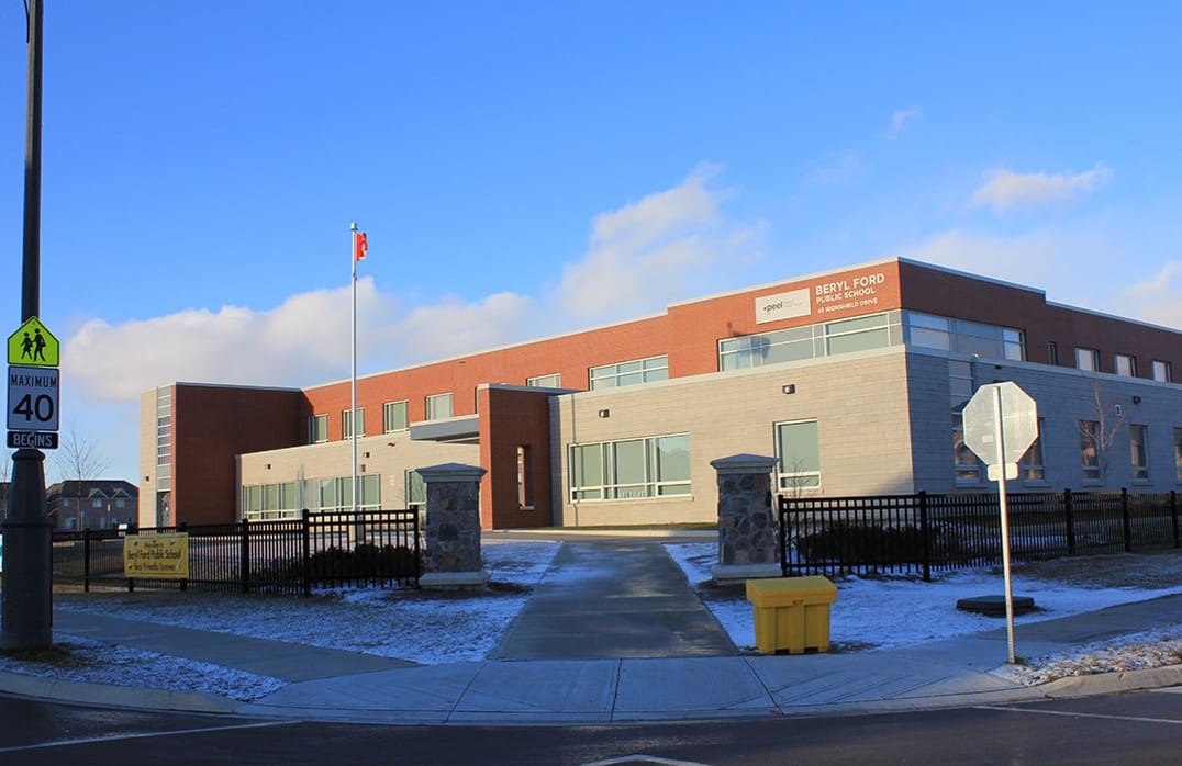 Modern school building with a Canadian flag, a pedestrian crossing sign, and a speed limit sign on a sunny day with clear blue sky.