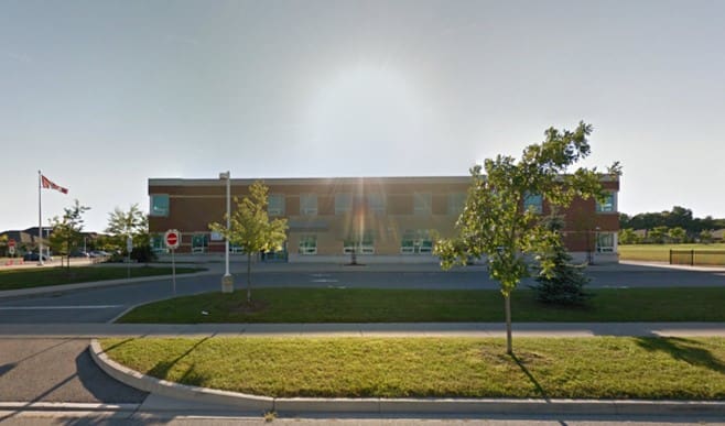 A view of a modern two-story school building with a flagpole and trees, under a clear sky.