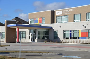 Modern school building with a colorful window design, clear skies, and an empty courtyard. Sign reads "Isaac Brock P.S.