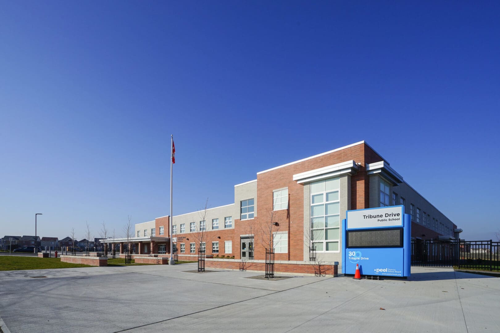 Exterior view of a modern brick school building under a clear blue sky, with street signs and a Canadian flag visible.